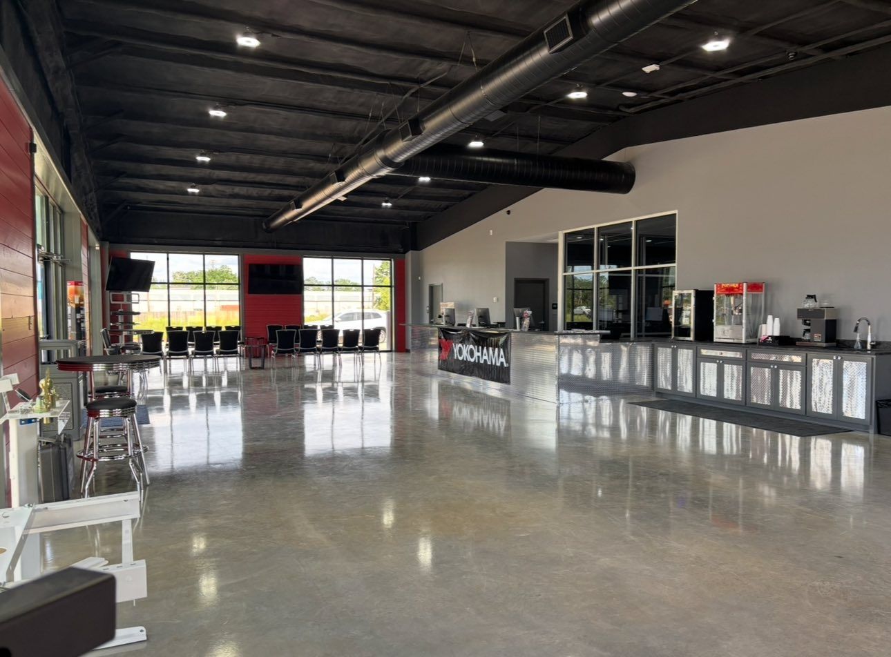 Empty modern showroom with polished concrete floor, black ceiling beams, and glass counters along the right side.