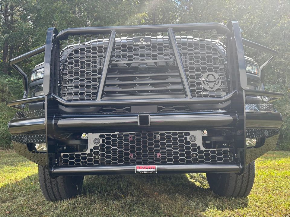 Front view of a black off-road truck with a heavy-duty grille guard, parked on grass in sunlight