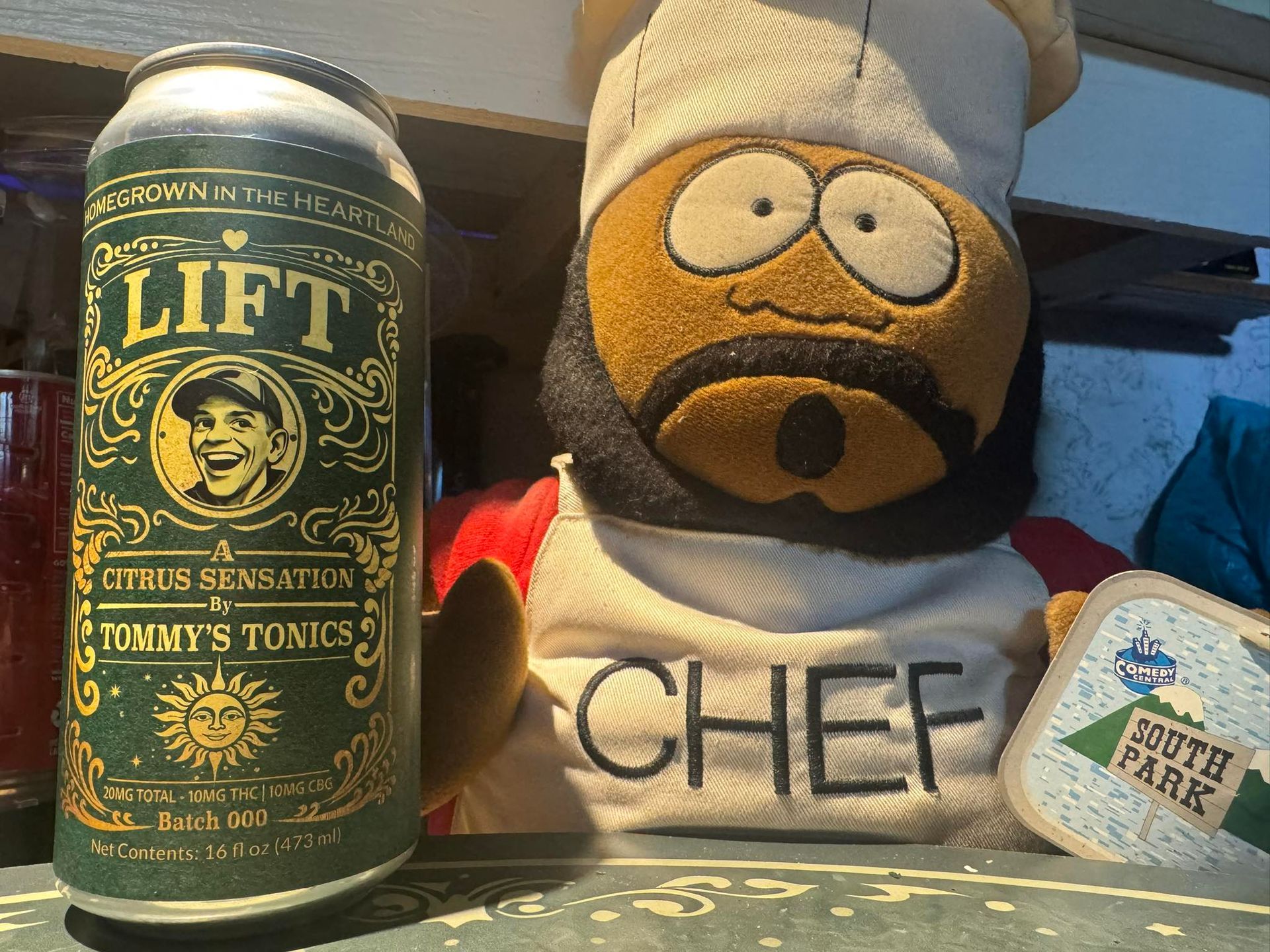 A green can beside a plush toy wearing a chef hat and shirt on a tabletop.