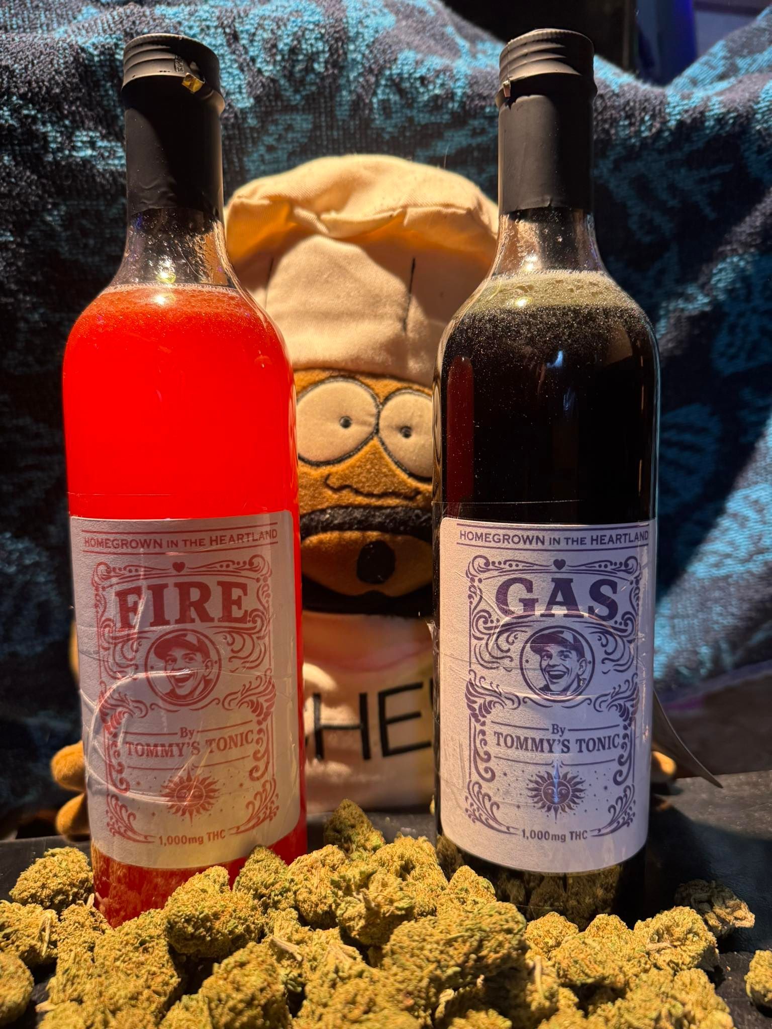 Two bottles labeled FIRE and GAS with a skull cap and a pile of cannabis buds in front.