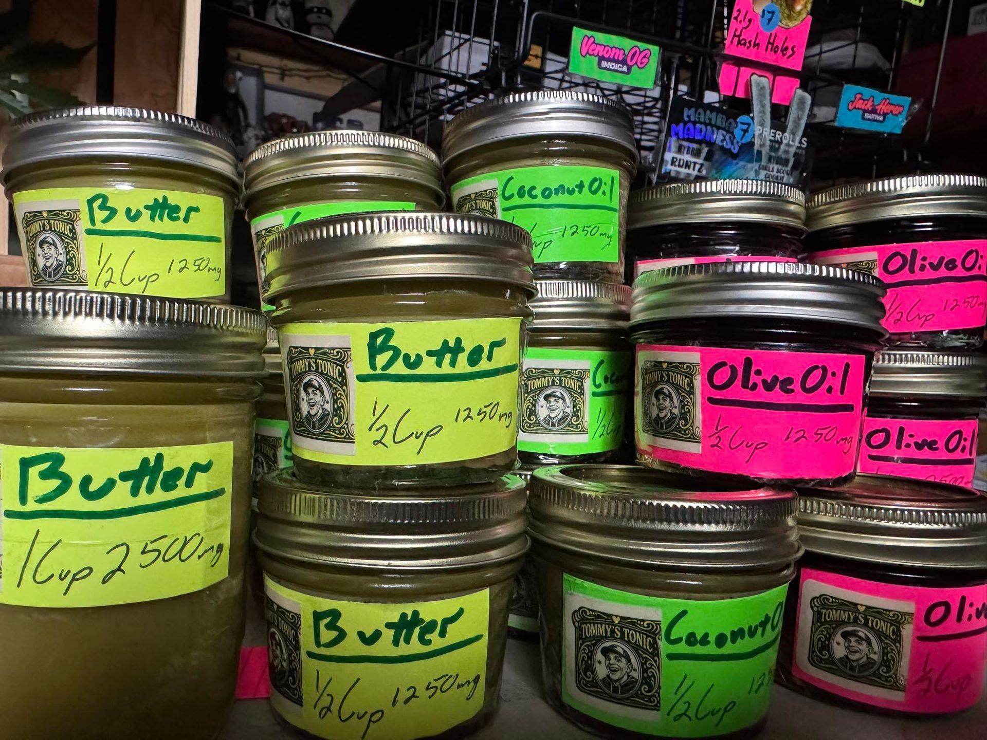 Rows of labeled jars of butter, coconut oil, and olive oil with bright neon notes in a market display