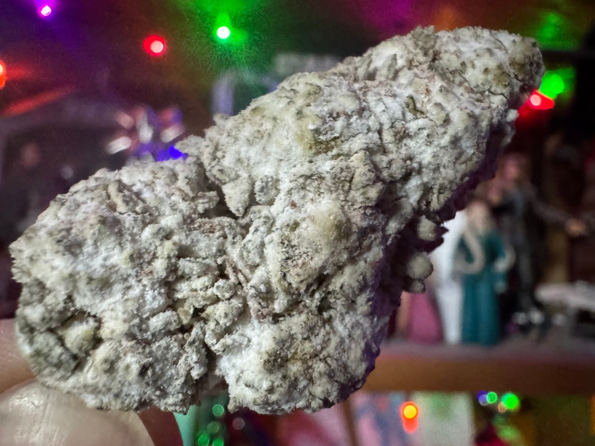 Close-up of a rough gray rock against a blurred, colorful indoor background with lights and people