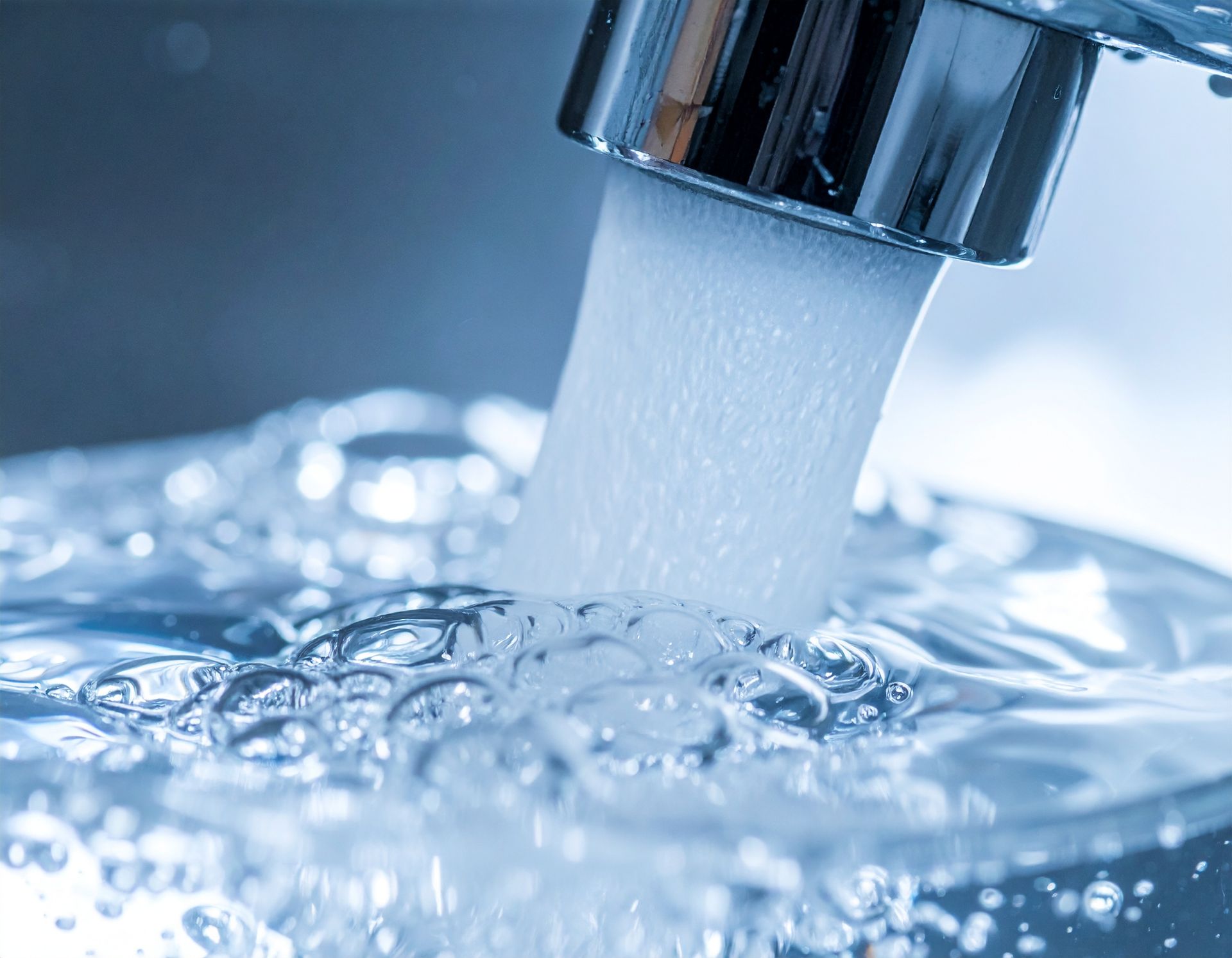 A person uses a handheld tool to remove a white plastic water filter housing over a kitchen sink.