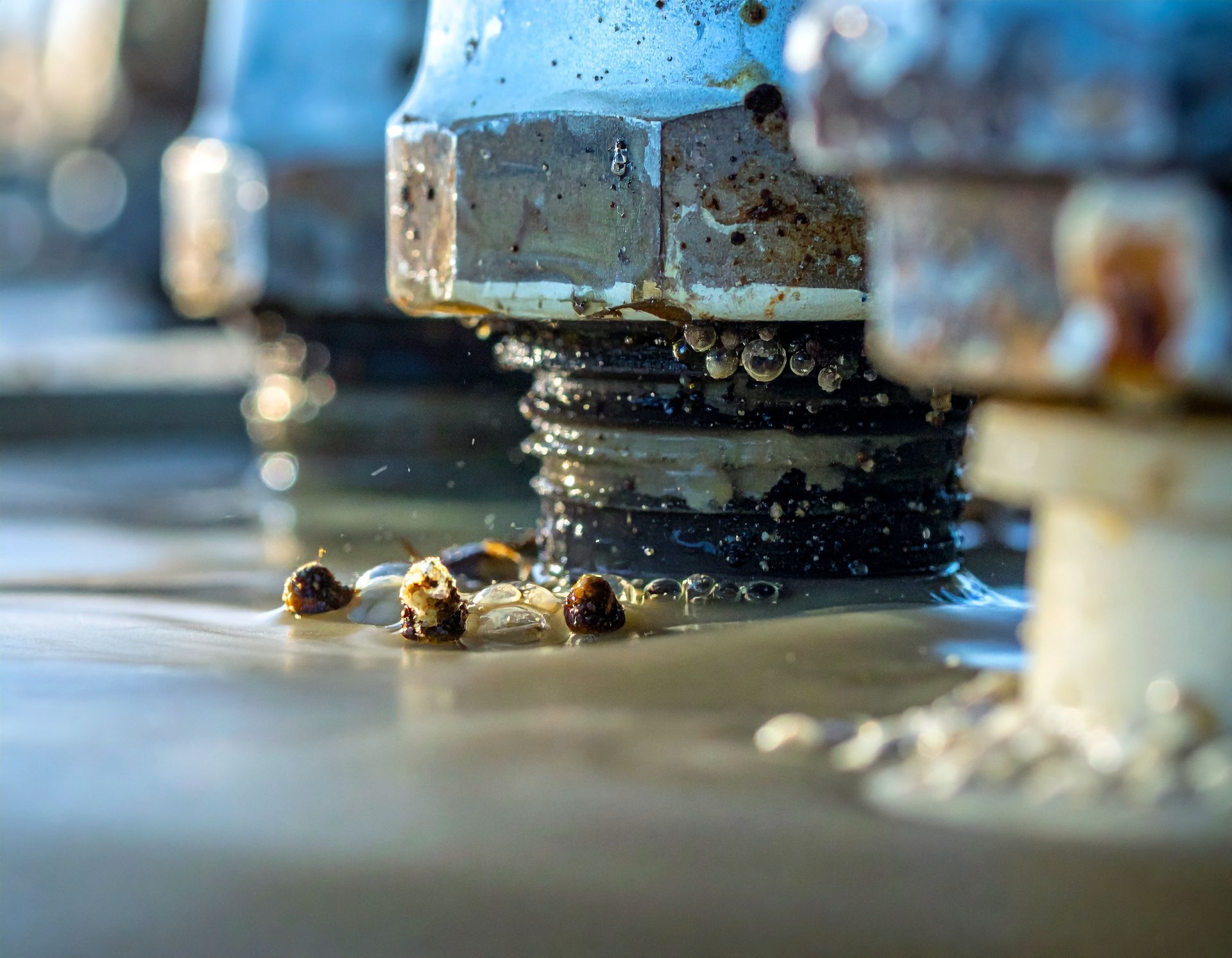 Close-up of threaded metal bolts partially submerged in murky, sediment-filled liquid with small debris floating nearby.