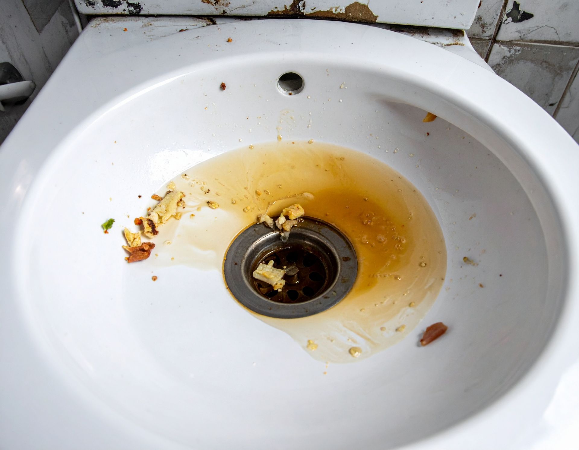 A white bathroom sink containing stagnant, brownish water and food debris clogging the drain.