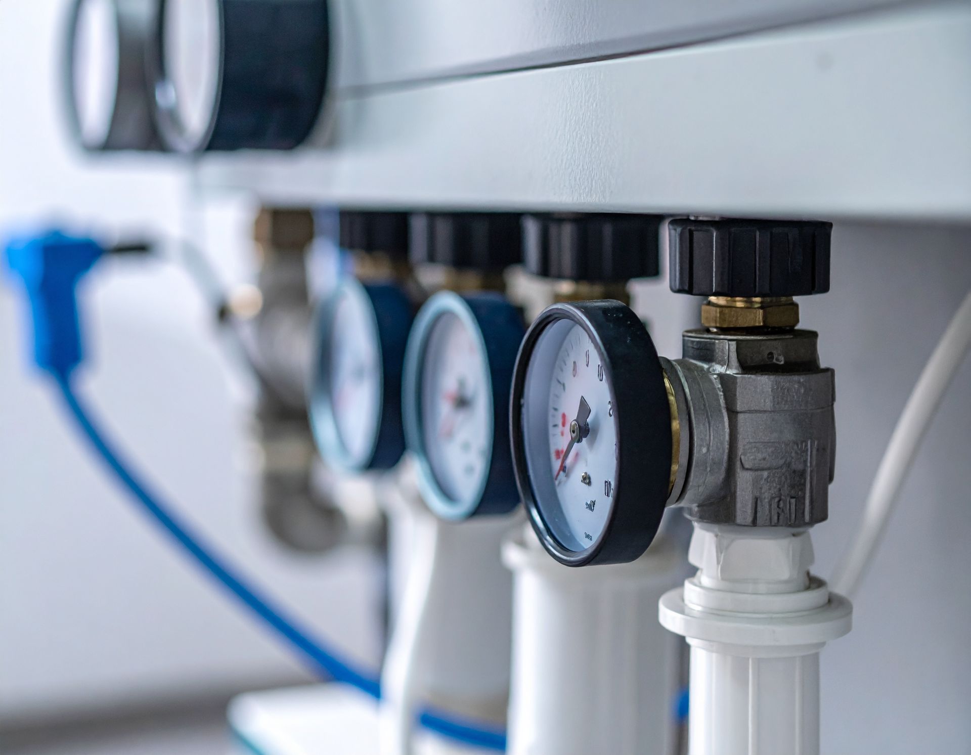 Close-up of a central heating manifold featuring multiple pressure gauges and black control valves on white pipes.