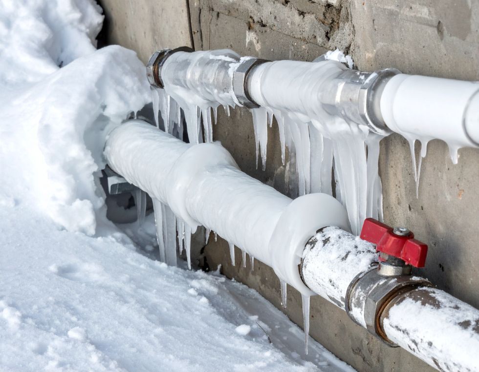 Frozen pipes covered in snow and icicles, red valve visible.