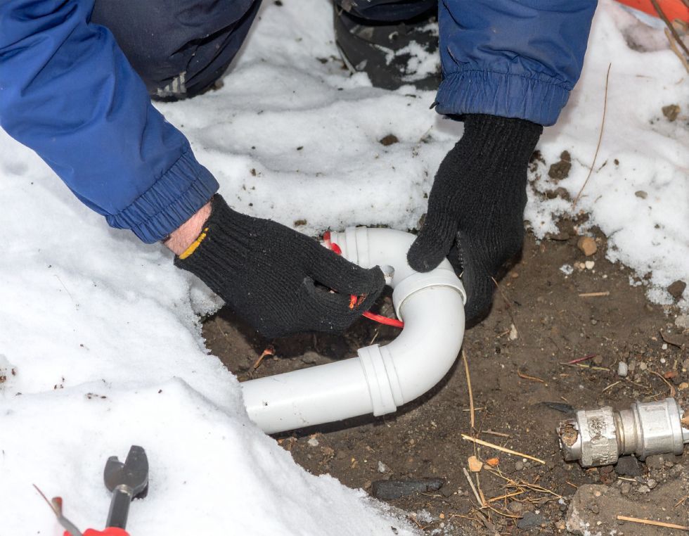 Person in gloves repairing white PVC pipe in snow.