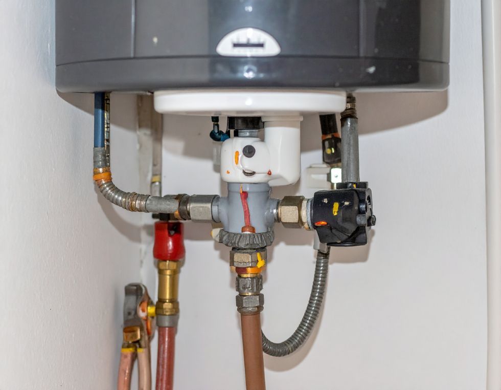 Close-up of a water heater with pipes and valves connected against a white wall.