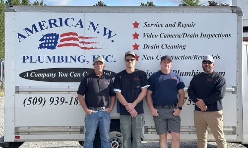 Four plumbers standing in front of an America N.H. Plumbing service truck and banner.
