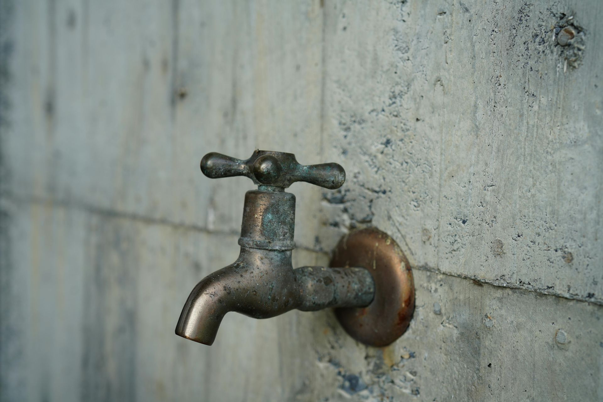 Brass faucet mounted on a rough concrete wall.