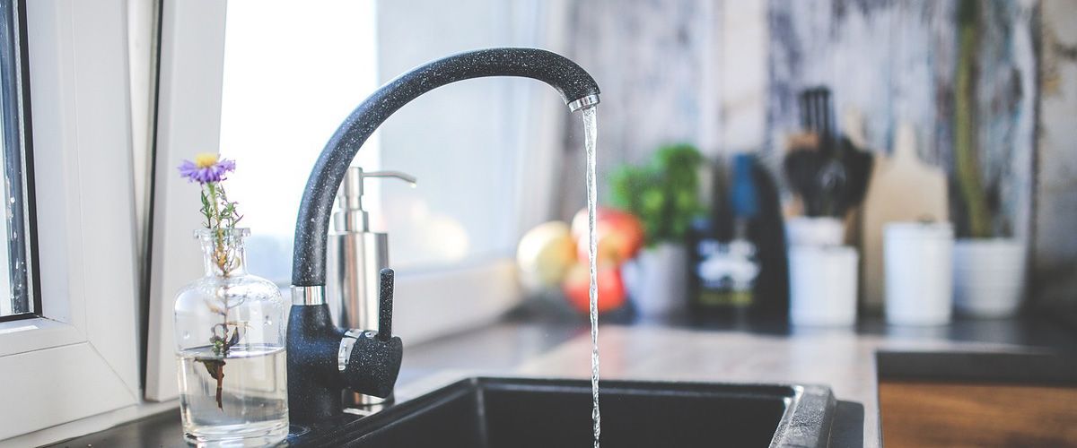 Water flowing from a black faucet into a black sink in a kitchen, flowers in a vase.