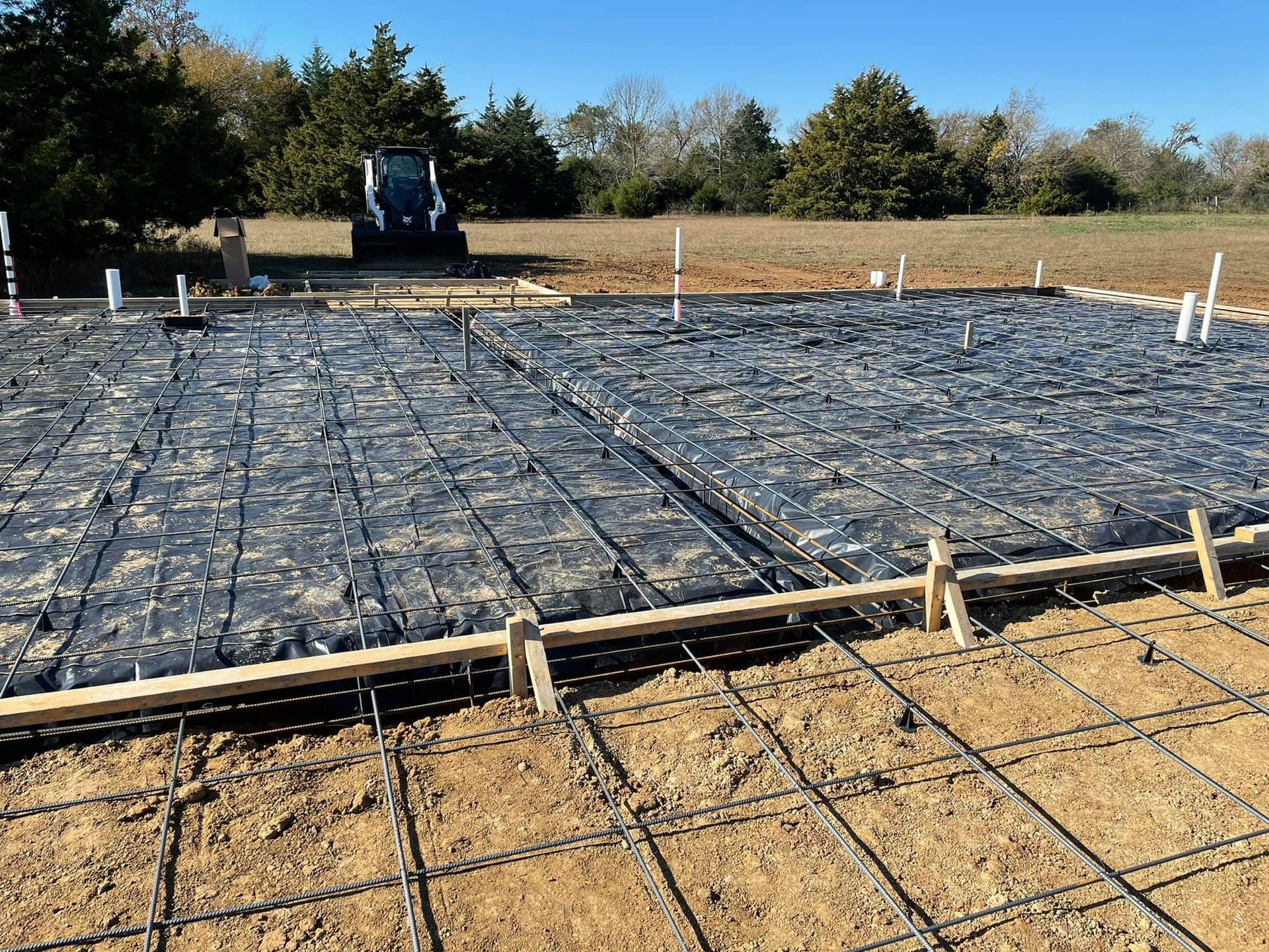 A concrete foundation is being built in a field with a tractor in the background.