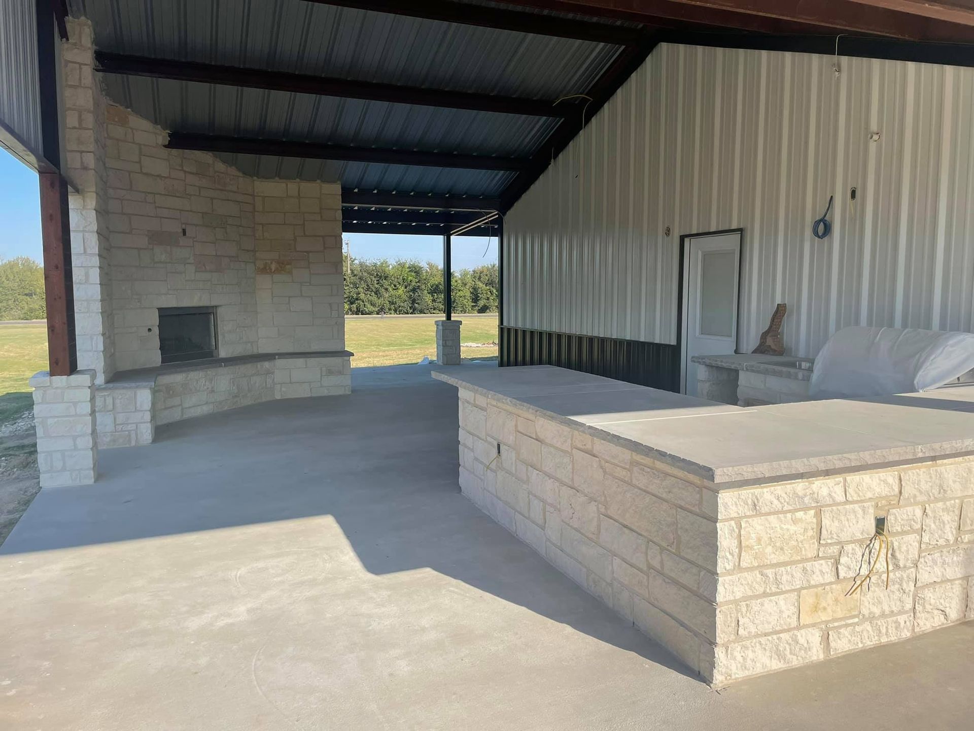 A covered patio area with a fireplace and a brick wall.
