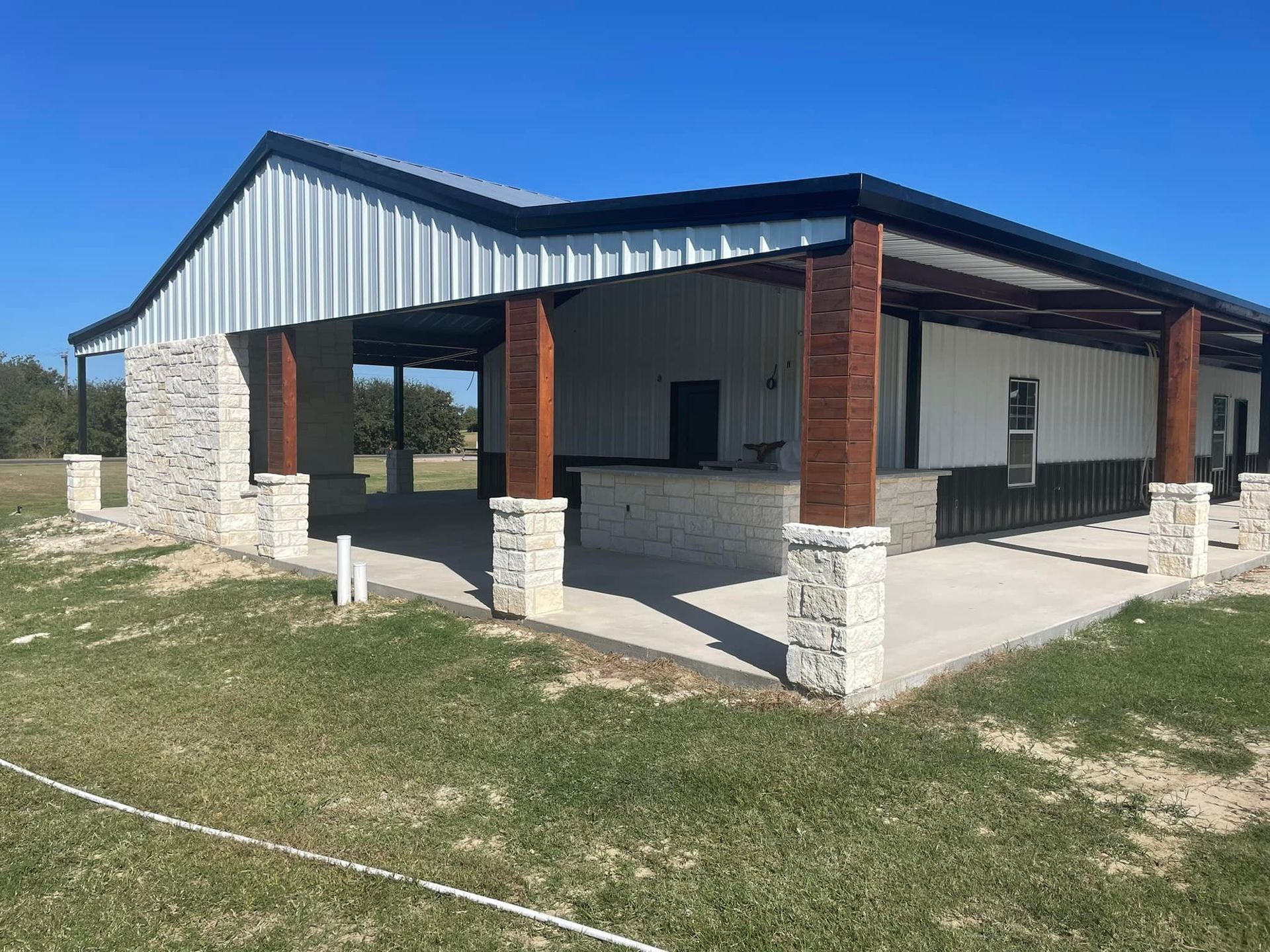 A large white building with wooden beams and pillars is sitting on top of a lush green field.