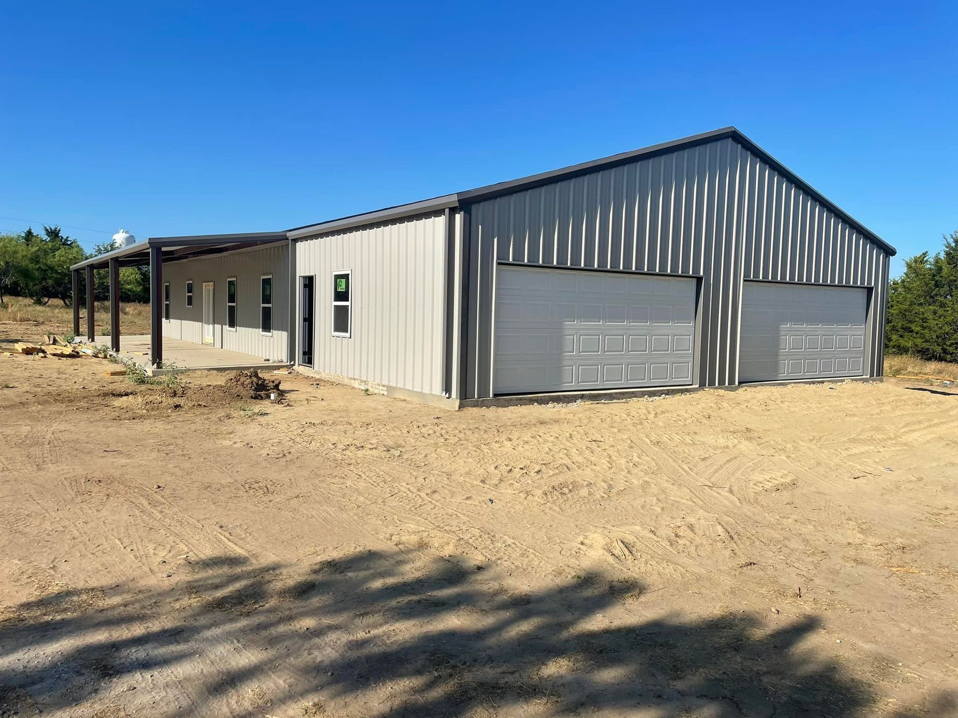 A large metal building with two garage doors is sitting in the middle of a dirt field.