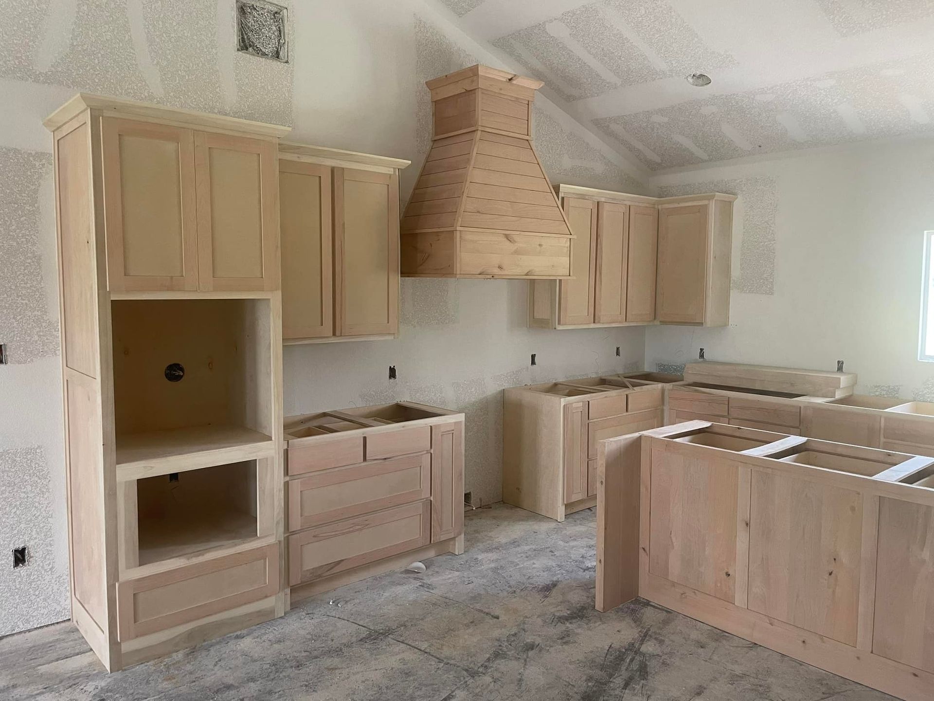 A kitchen under construction with wooden cabinets and a hood.