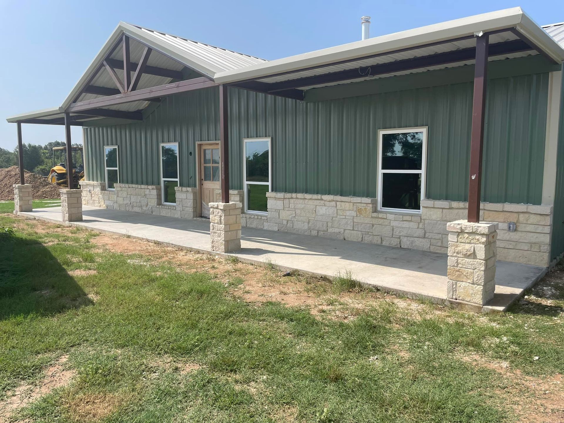 A large green metal building with a porch and windows.
