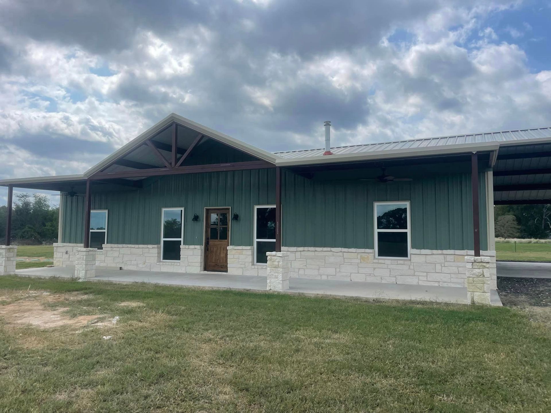 A large green house with a porch is sitting on top of a lush green field.