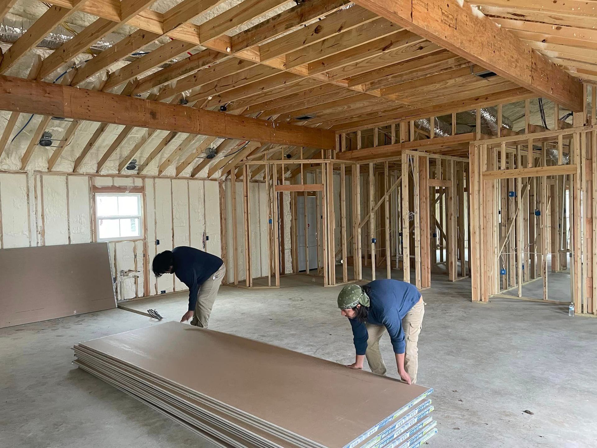 Two men are working on a stack of drywall in a room under construction.