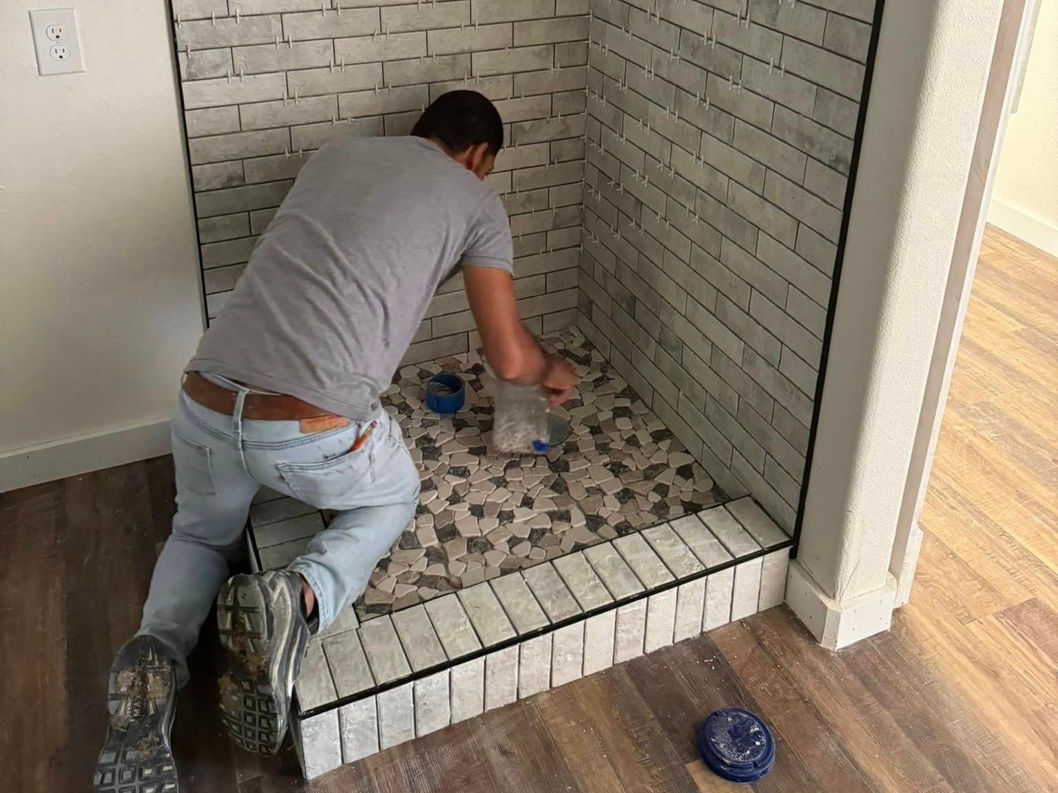 A man is kneeling on the floor in a shower stall.
