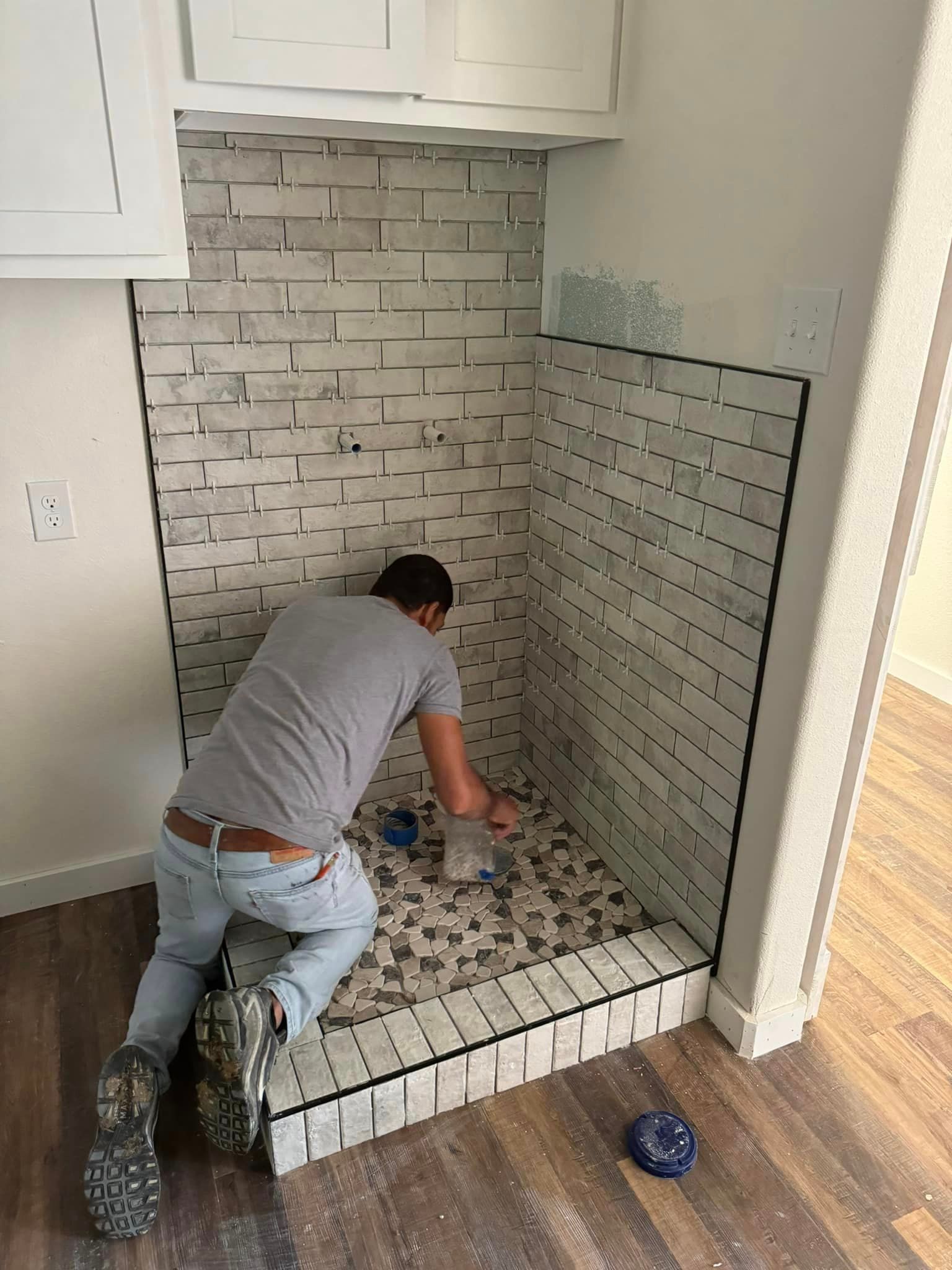 A man is kneeling down in front of a brick wall in a bathroom.