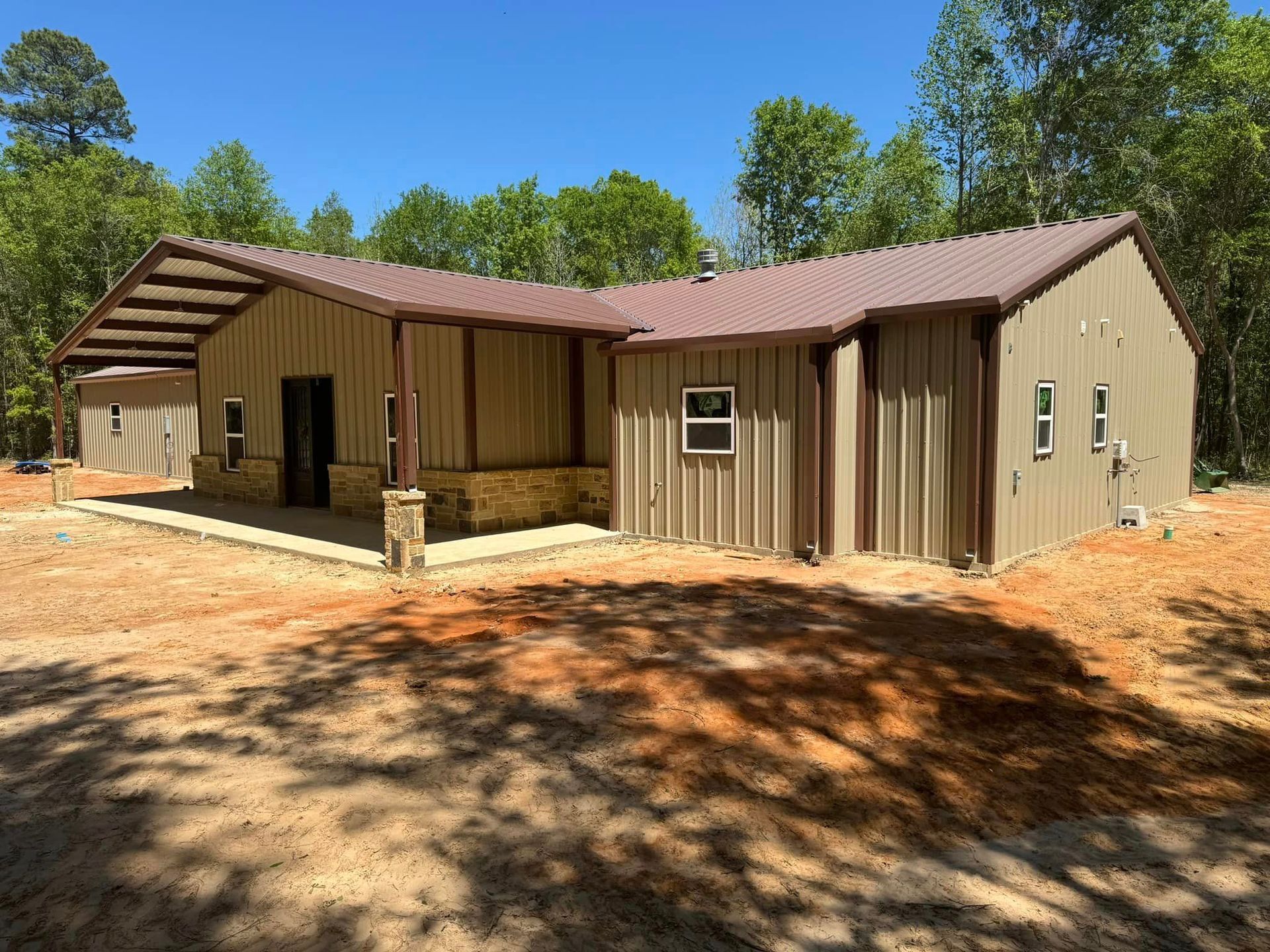 A large metal building with a red roof is surrounded by trees.