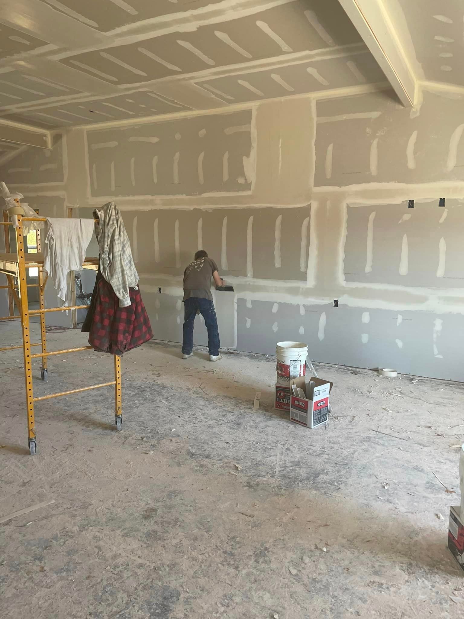 A man is standing in a room painting a wall.