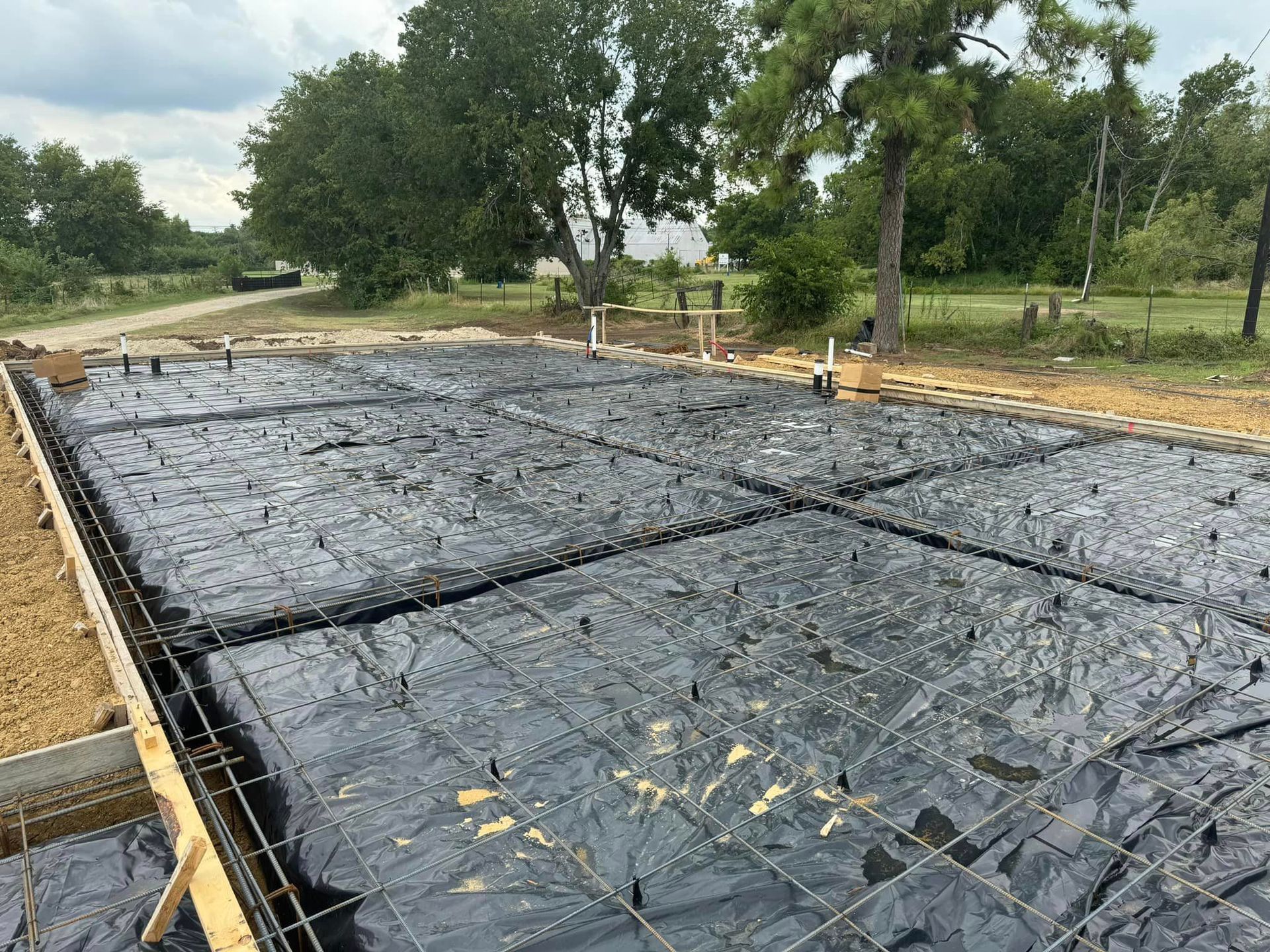 A concrete foundation is being built in a field with trees in the background.