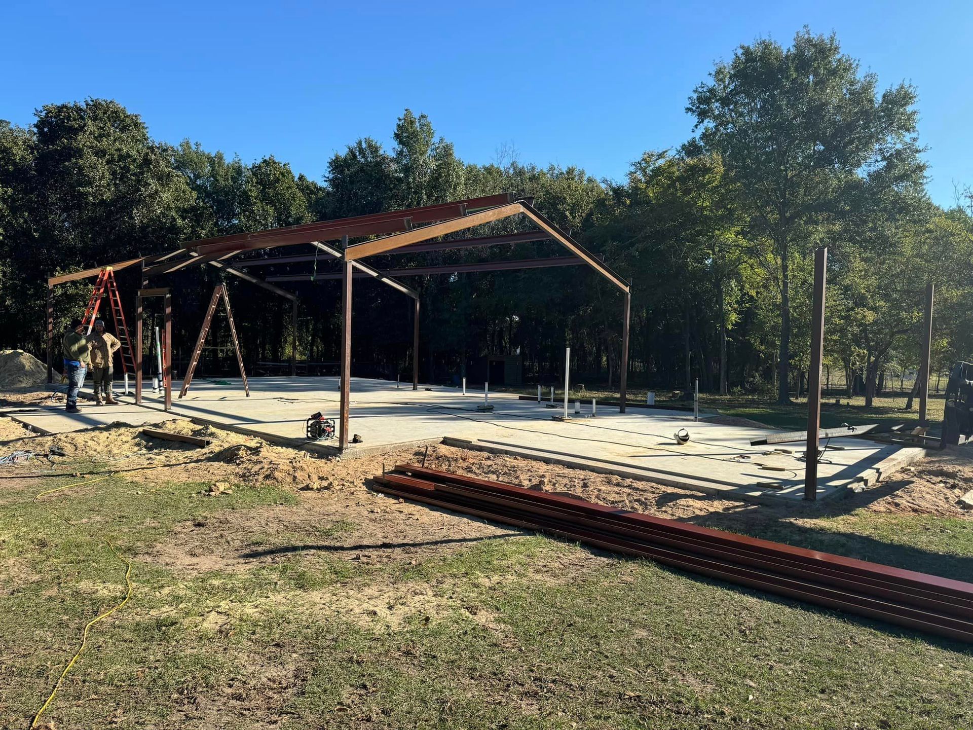 A large metal structure is being built in a field with trees in the background.