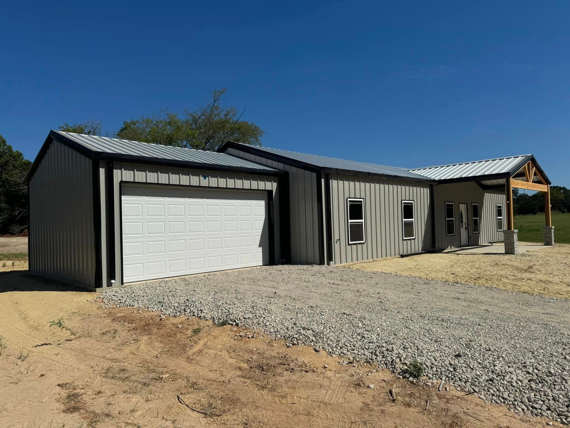A large metal building with two garage doors is sitting on top of a gravel lot.