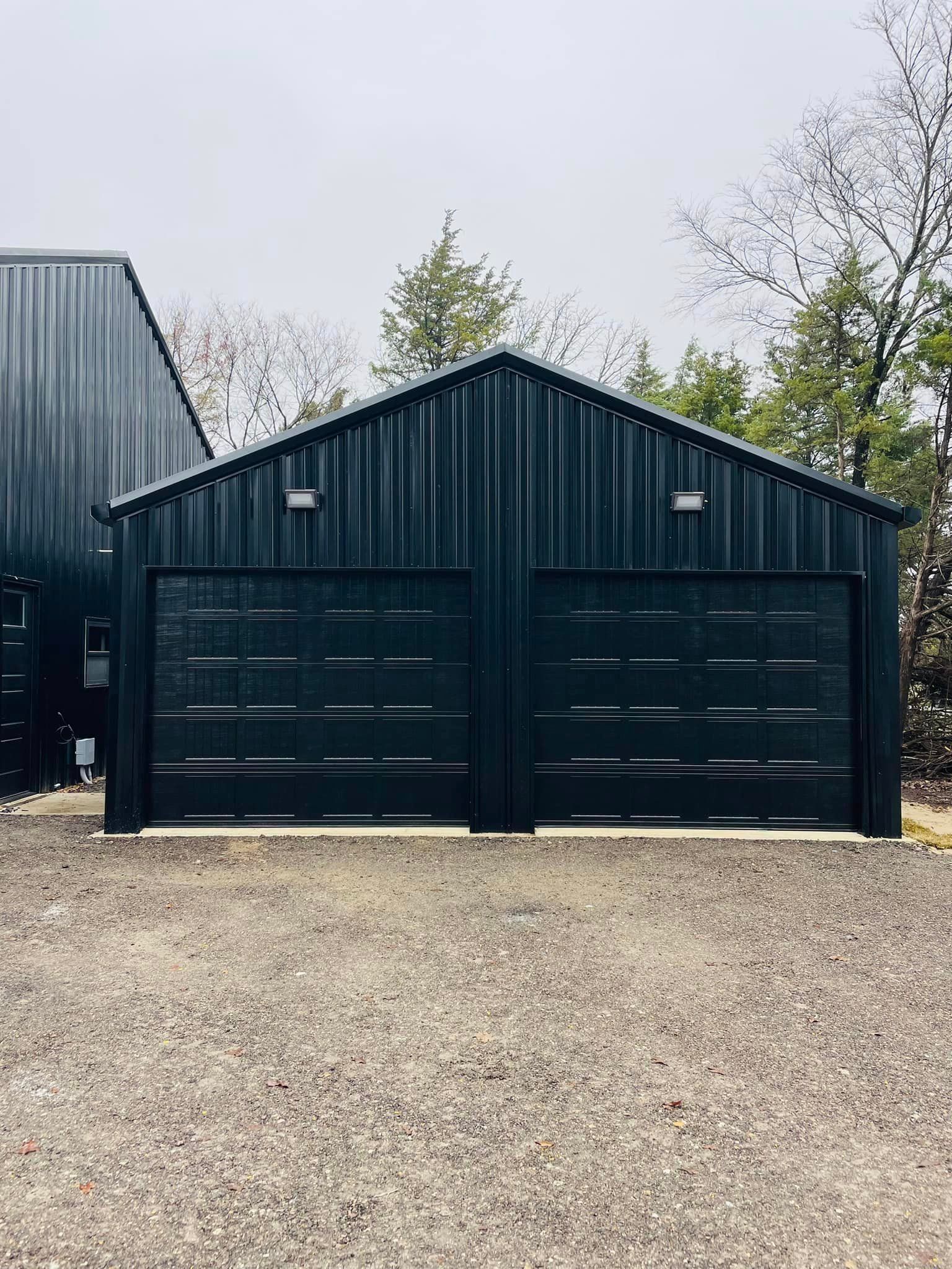 A black garage with two garage doors is sitting on top of a gravel driveway.