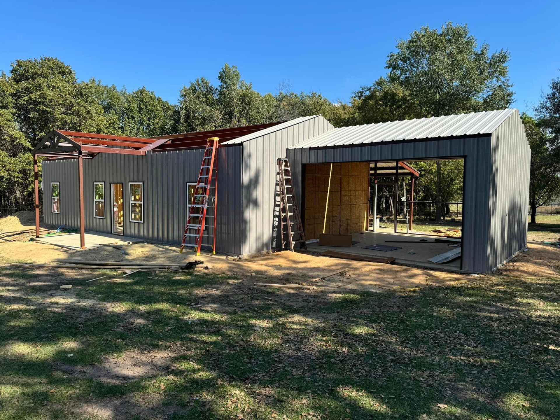 A large metal building is being built in the middle of a grassy field.
