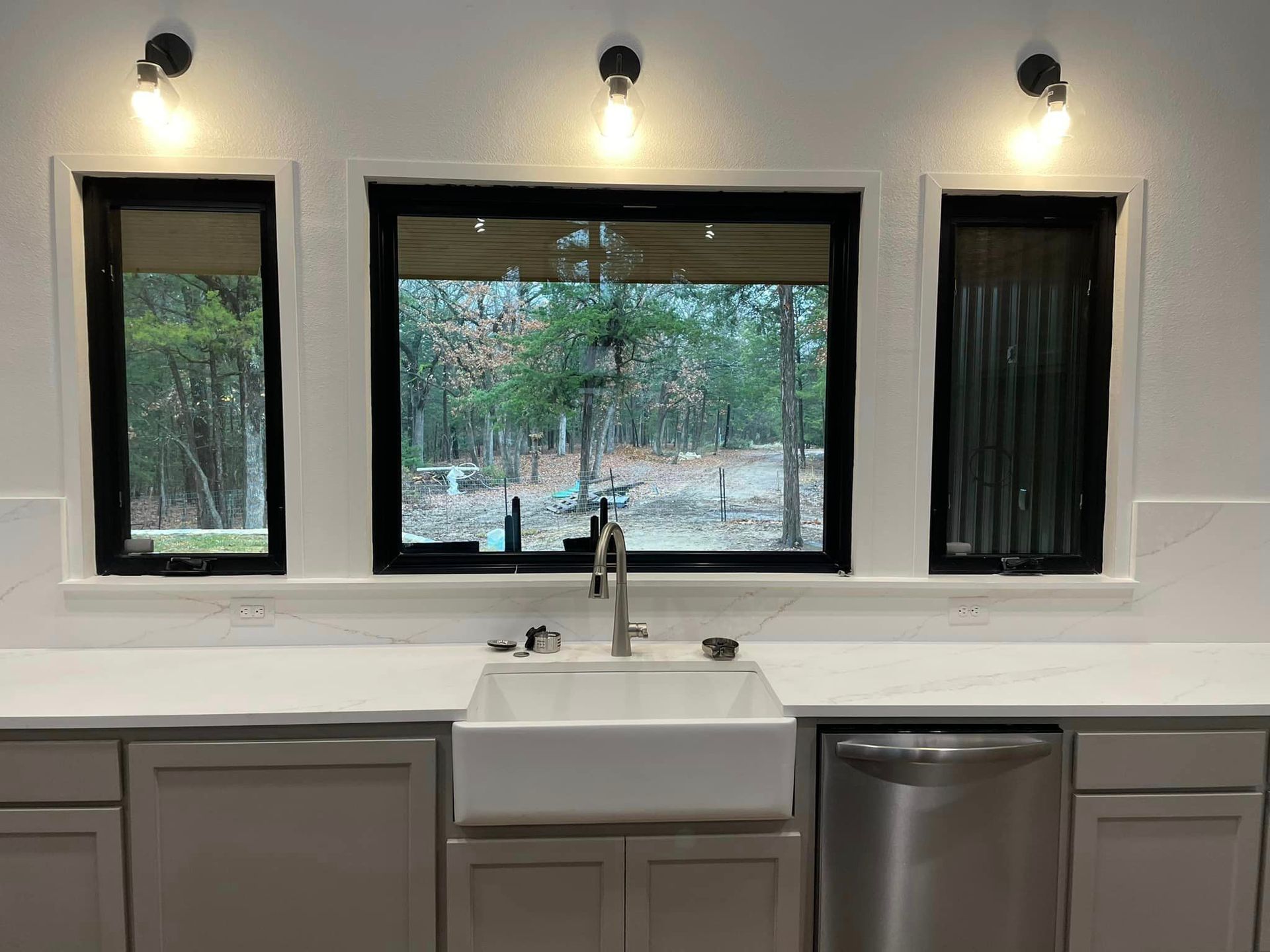 A kitchen with a sink , dishwasher , and three windows.