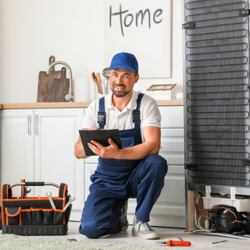 A man is kneeling down in front of a refrigerator while holding a tablet.