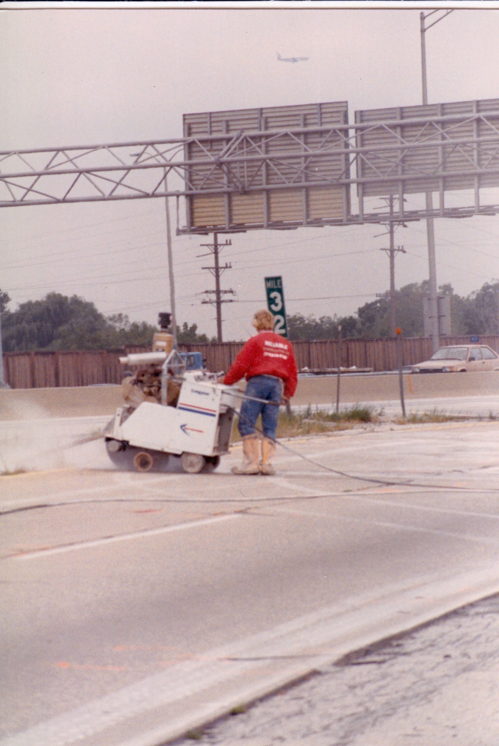 A man in a red shirt is standing next to a machine on the side of the road