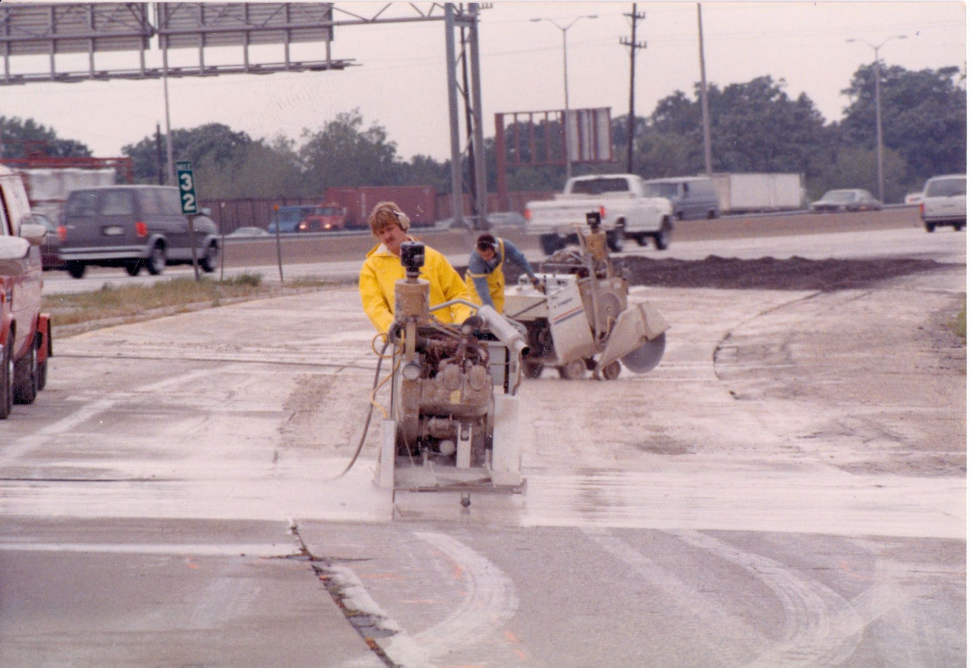 A man in a yellow jacket is using a machine to cut concrete