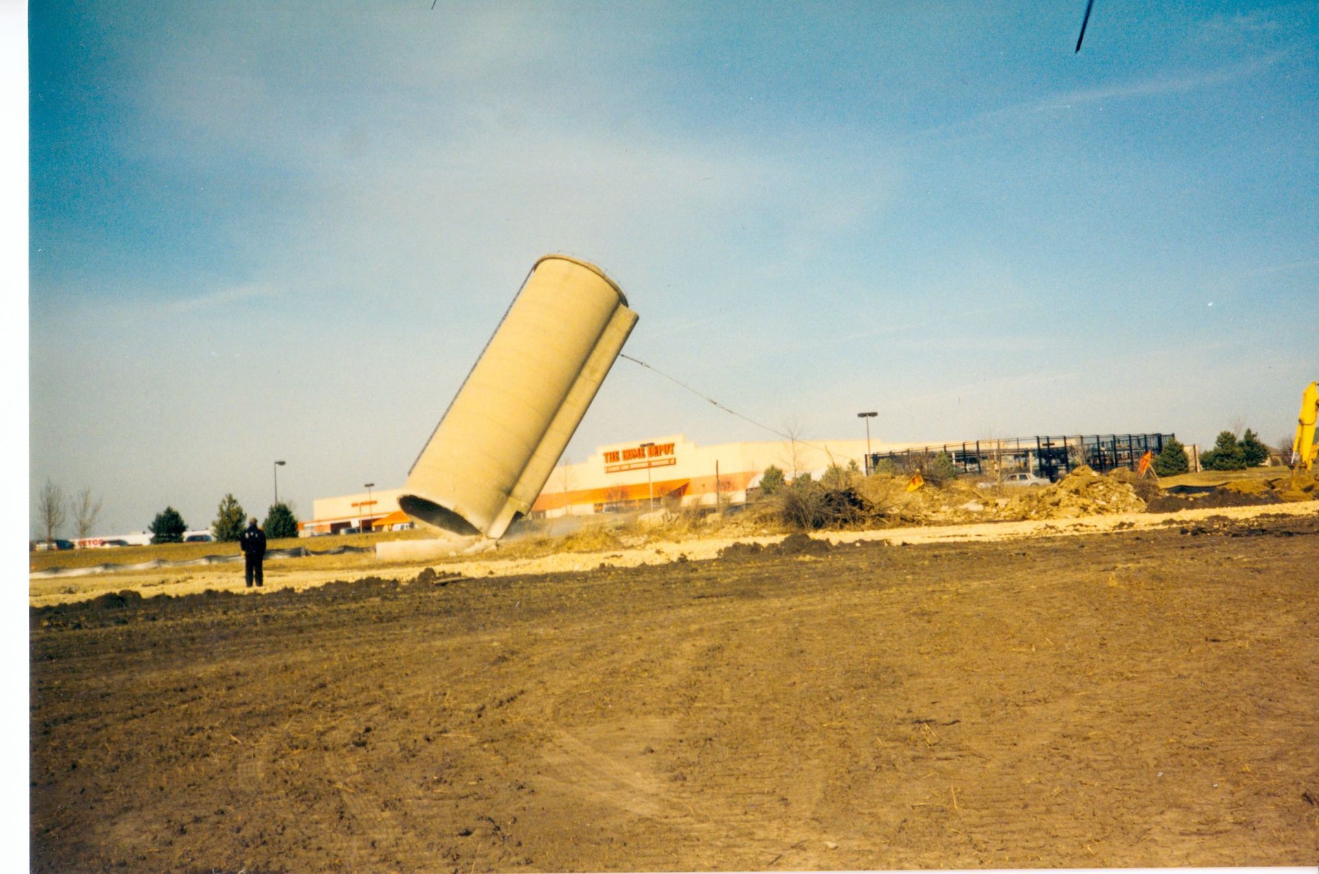 A man stands in a field in front of a building that says home depot