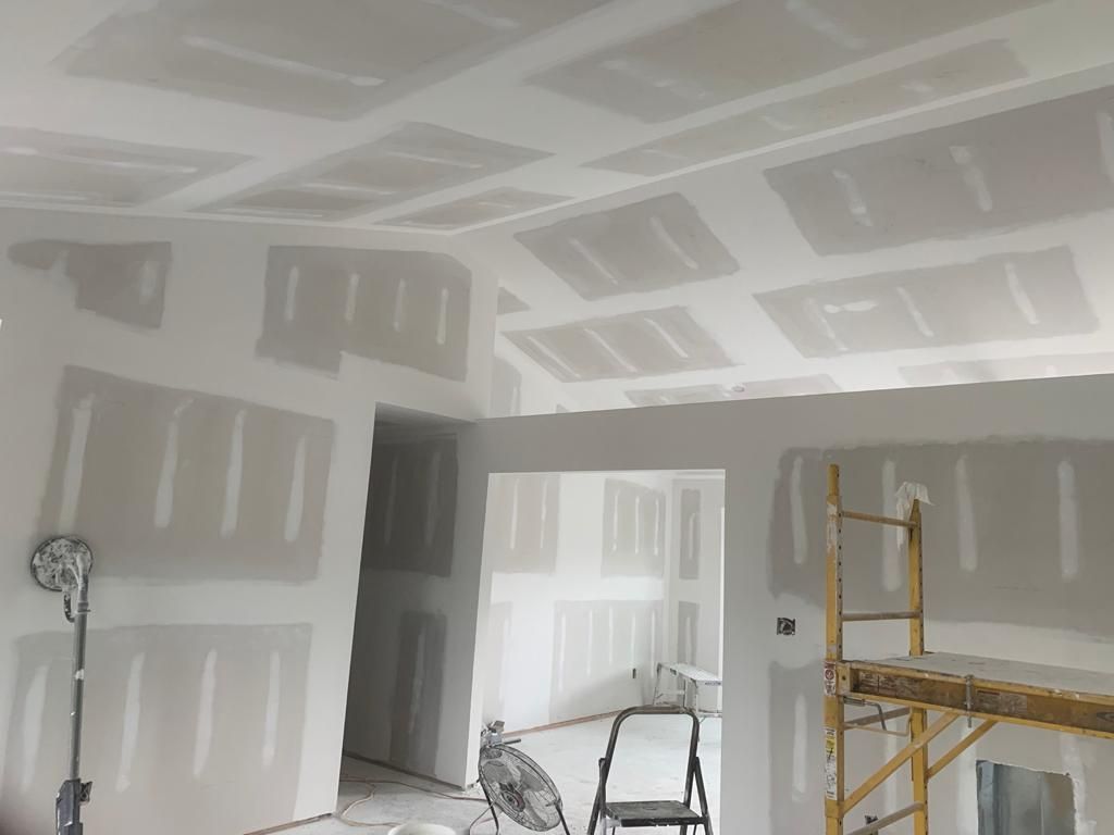 Interior under construction with drywall installed on walls and ceiling, and scaffolding.