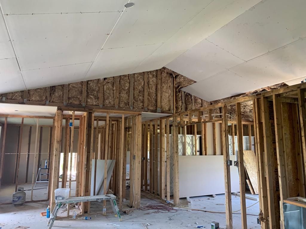 Interior view of a house under construction: exposed wooden framing, drywall on ceiling, insulation visible.