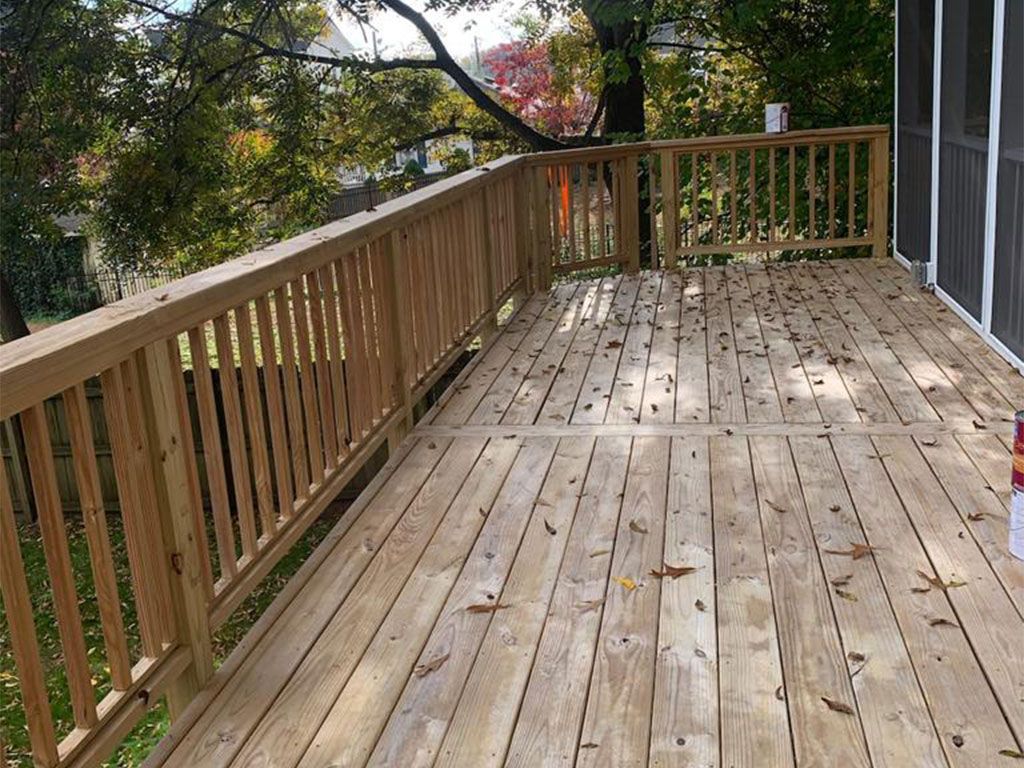 Wooden deck with railing and scattered leaves, outdoors.