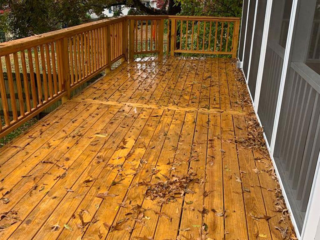 Wooden deck with fallen leaves, part of a house.