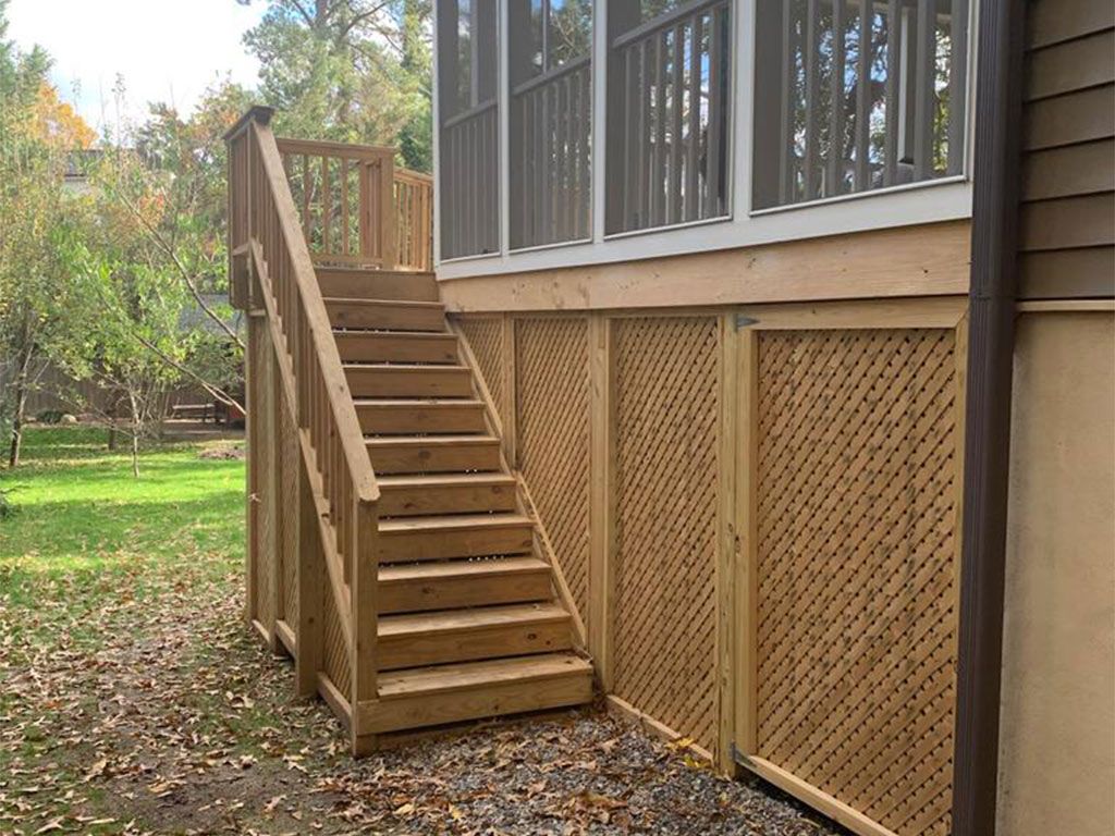 Wooden staircase leading up to a screened porch, with lattice skirting on the ground level, set in a grassy yard.