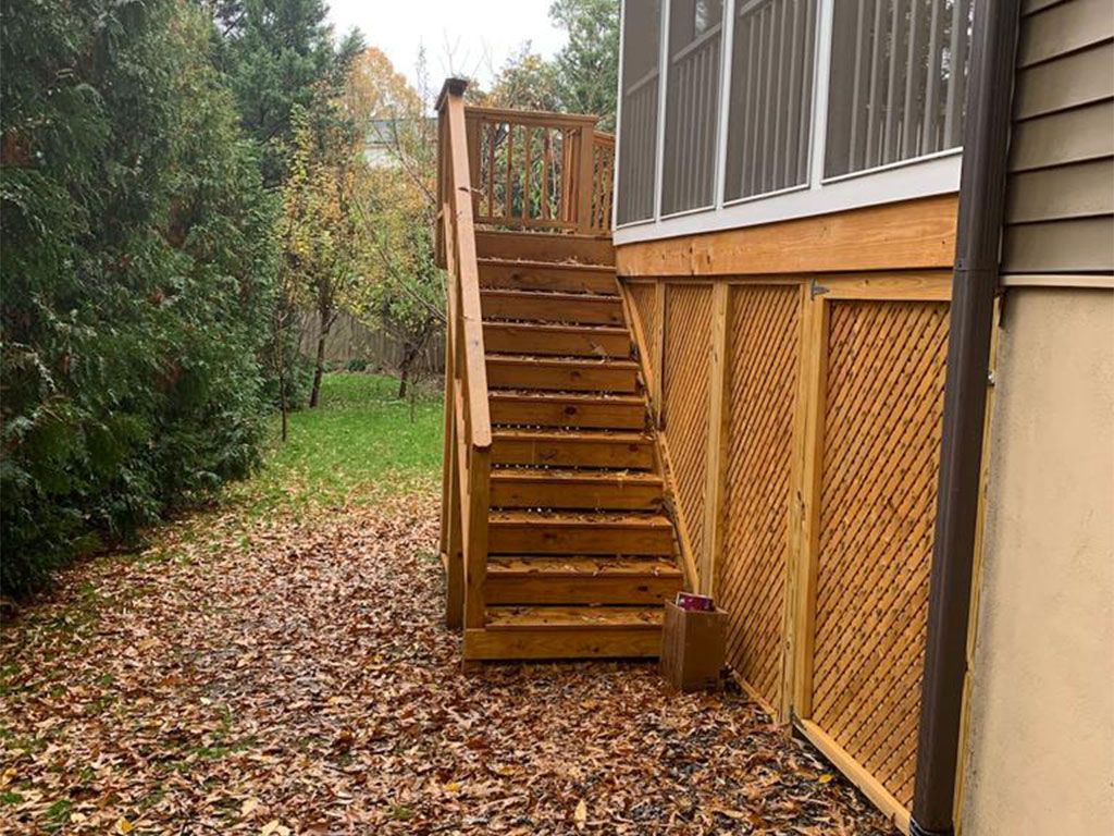 Wooden outdoor stairs leading to a screened porch, with fallen leaves on the ground.