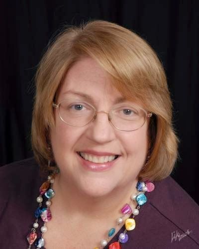 A woman wearing glasses and a colorful necklace smiles for the camera