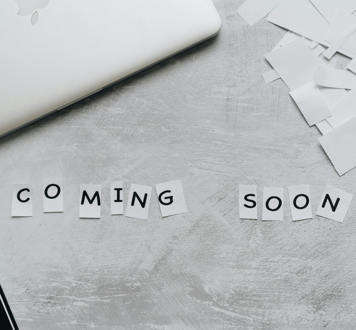 The word coming soon is written on a piece of paper on a table next to a laptop.