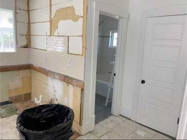 Renovated kitchen with bare drywall, white tile floor, black trash bag, and a closed white door