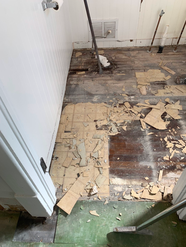 Damaged floor with peeling beige linoleum and exposed dark wood in a narrow room.
