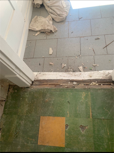 Threshold between a green floor and gray tiled area, with bags and debris near a worn doorway.