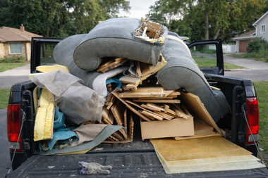 The back of a black pickup truck filled with deconstructed, gray upholstered furniture and wooden scraps.